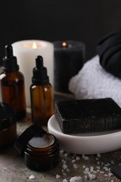 Spa composition. Black soap bar, sea salt, jar of cream and towels on table