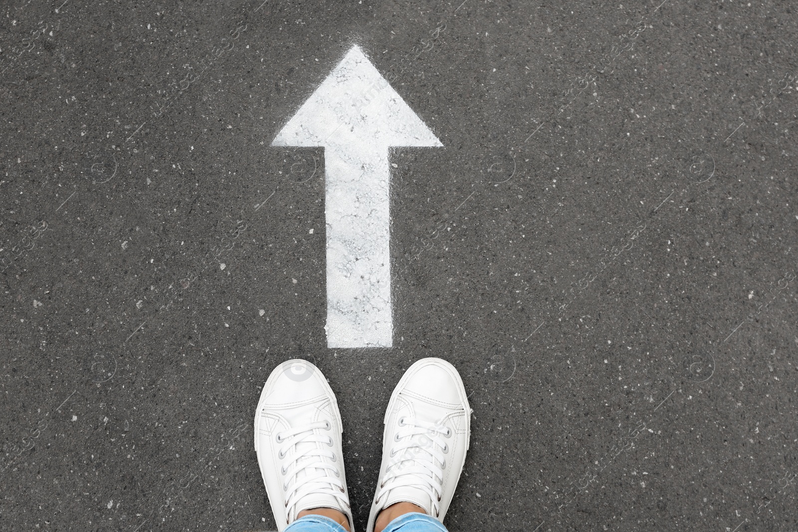 Photo of Woman standing near arrow on asphalt, top view. Choice concept