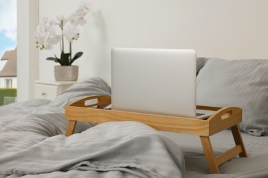 Photo of Wooden tray table with laptop and smartphone on bed indoors