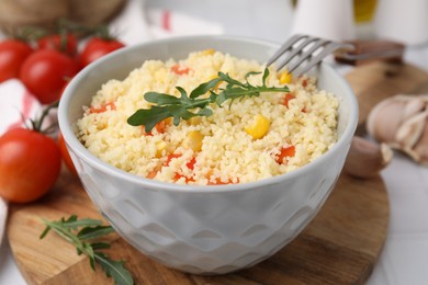 Photo of Bowl of tasty couscous with pepper, corn, arugula and fork on white table, closeup