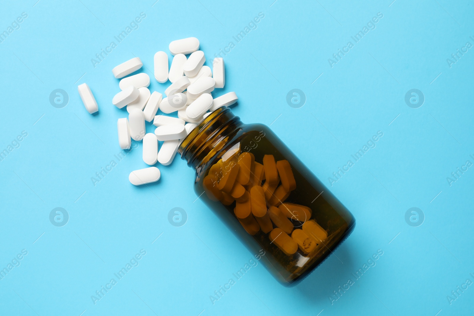 Photo of Bottle and vitamin capsules on light blue background, top view