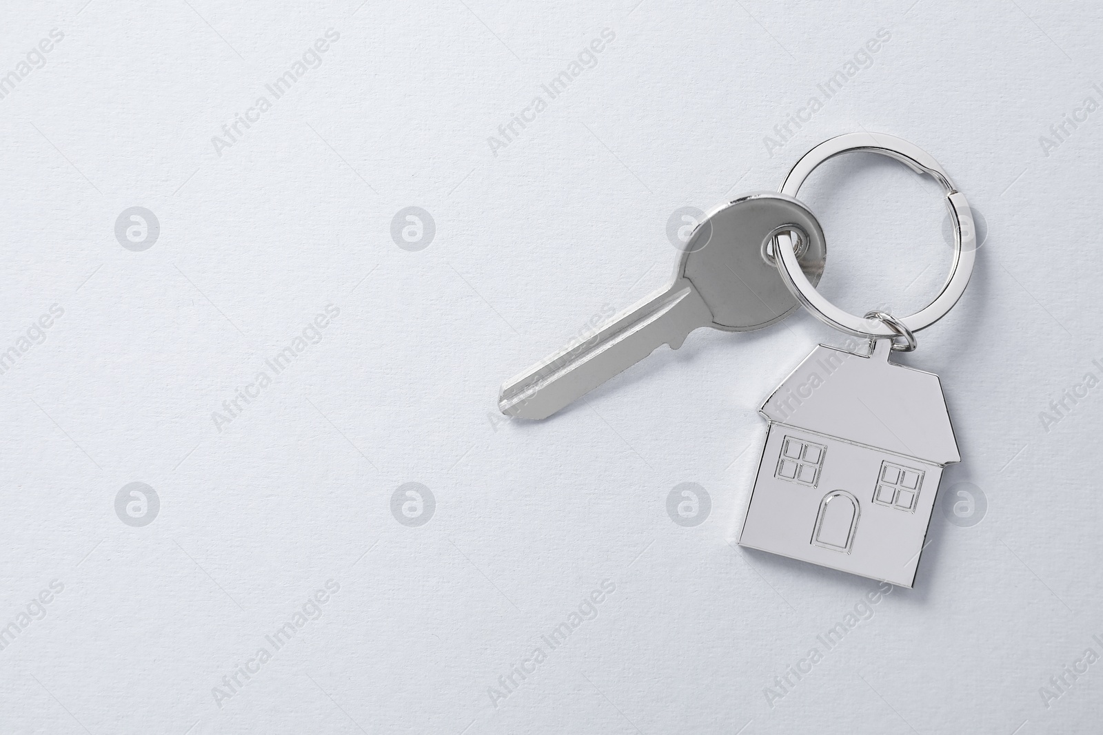 Photo of Key with keychain in shape of house on light background, top view. Space for text