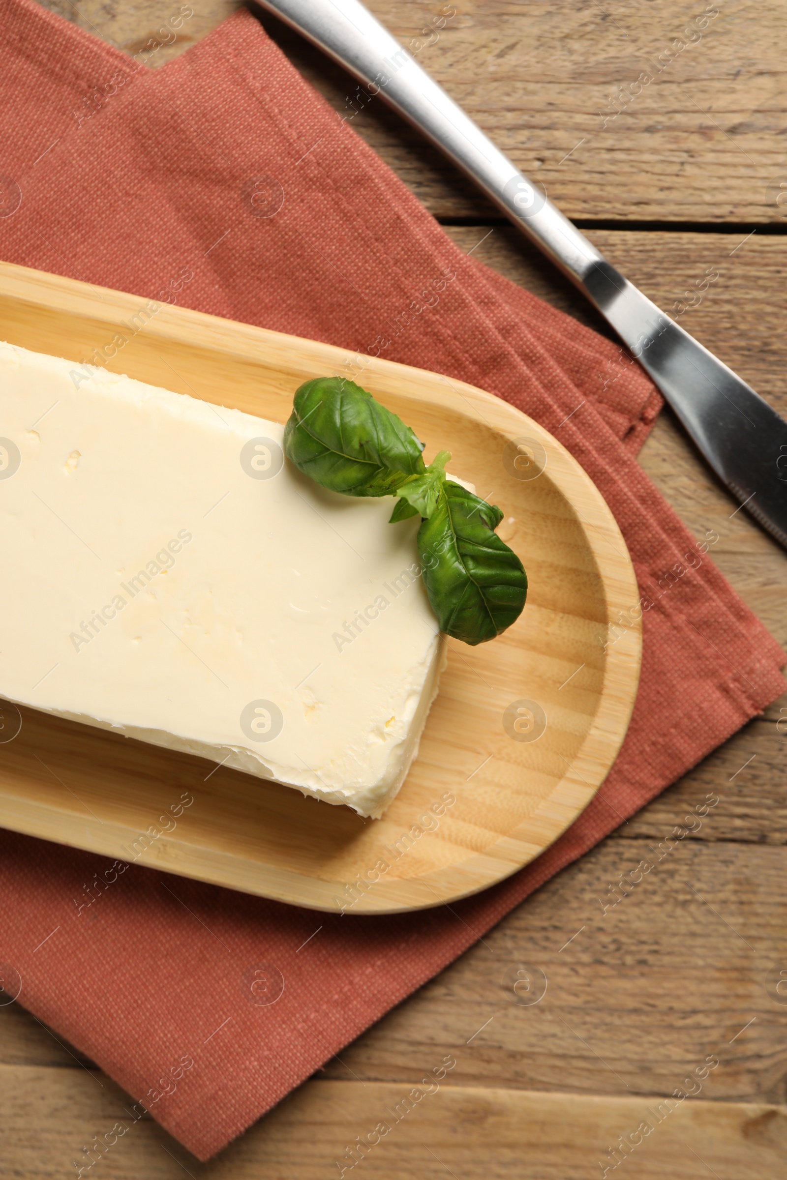 Photo of Block of tasty butter with basil and knife on wooden table, top view