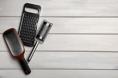 Photo of Different modern graters on white wooden table, flat lay. Space for text