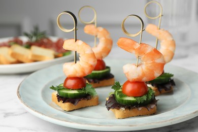 Photo of Tasty canapes with shrimps, cucumber, greens and tomatoes on white table, closeup