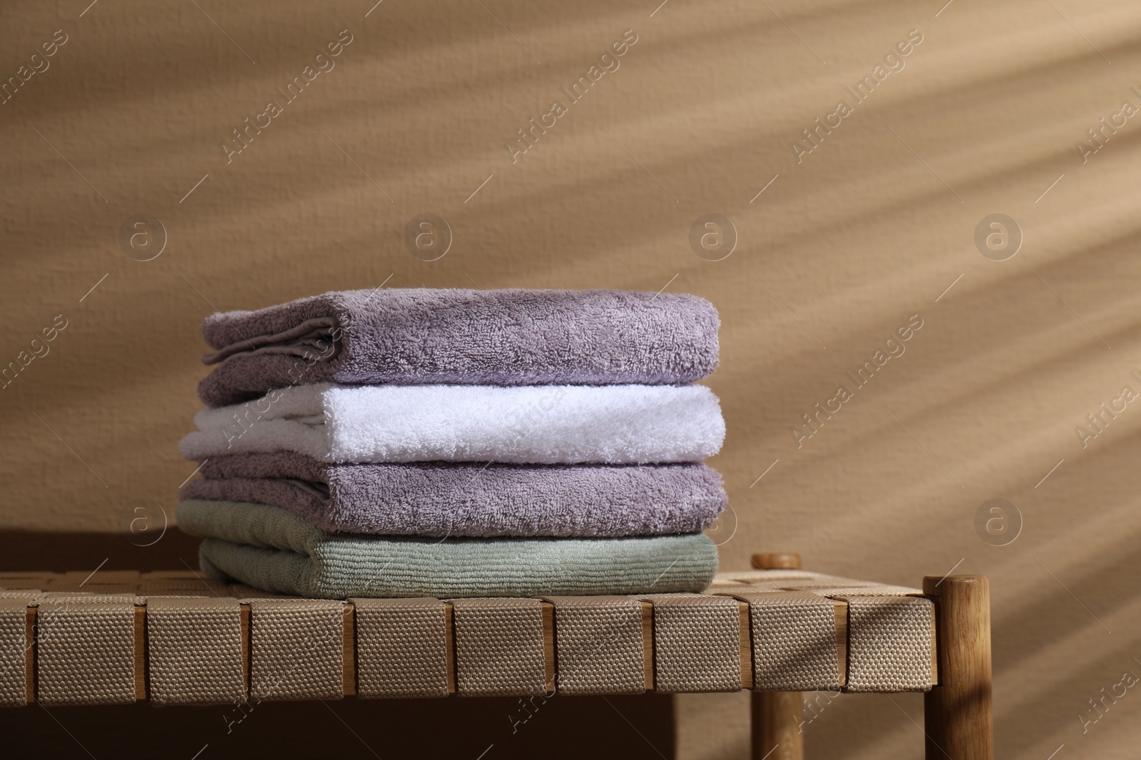 Photo of Stacked terry towels on wicker bench near beige wall