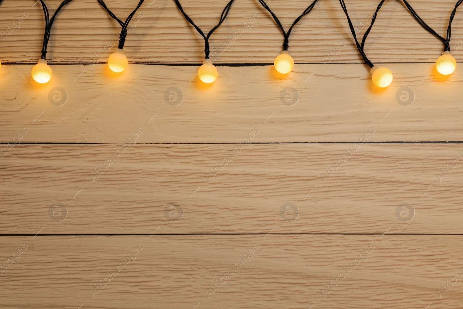 Photo of Glowing festive lights on wooden background, top view. Space for text