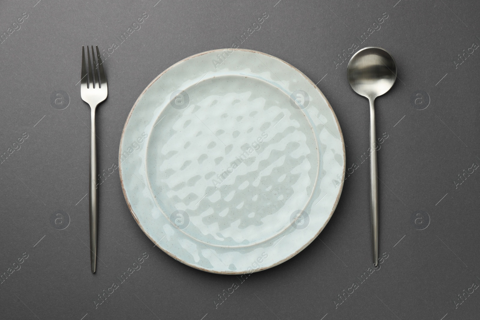 Photo of Clean plate, fork and spoon on grey background, top view