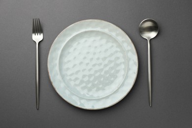 Photo of Clean plate, fork and spoon on grey background, top view
