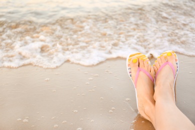 Photo of Closeup of woman with stylish flip flops on sand near sea, space for text. Beach accessories