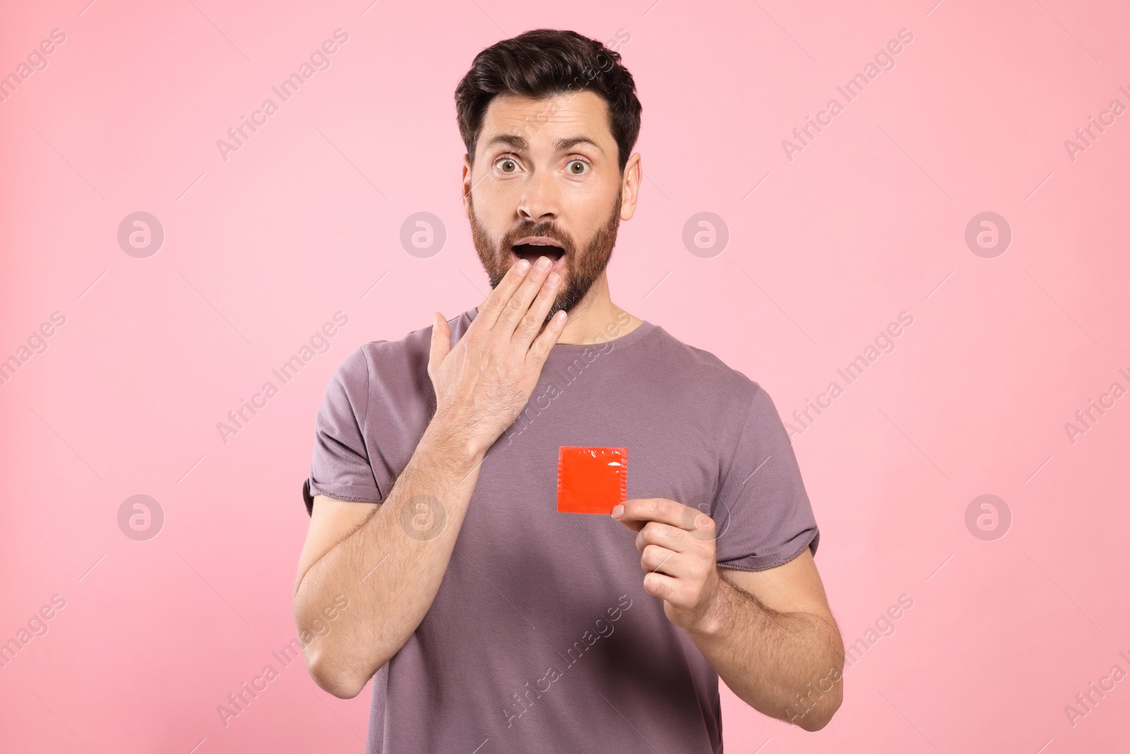 Photo of Emotional man holding condom on pink background. Safe sex