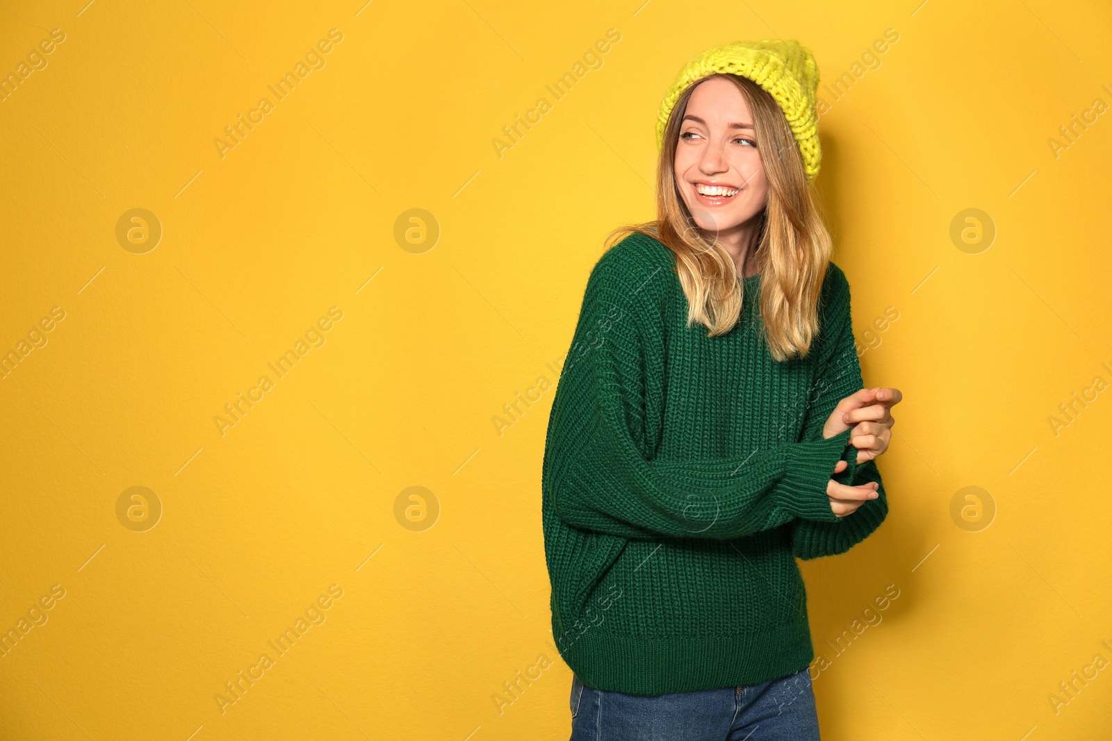 Image of Happy young woman wearing warm sweater and knitted hat on yellow background. Space for text