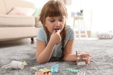 Photo of Little child taking pill on floor at home. Danger of medicament intoxication
