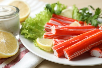 Photo of Delicious crab sticks with lemon and lettuce on table, closeup