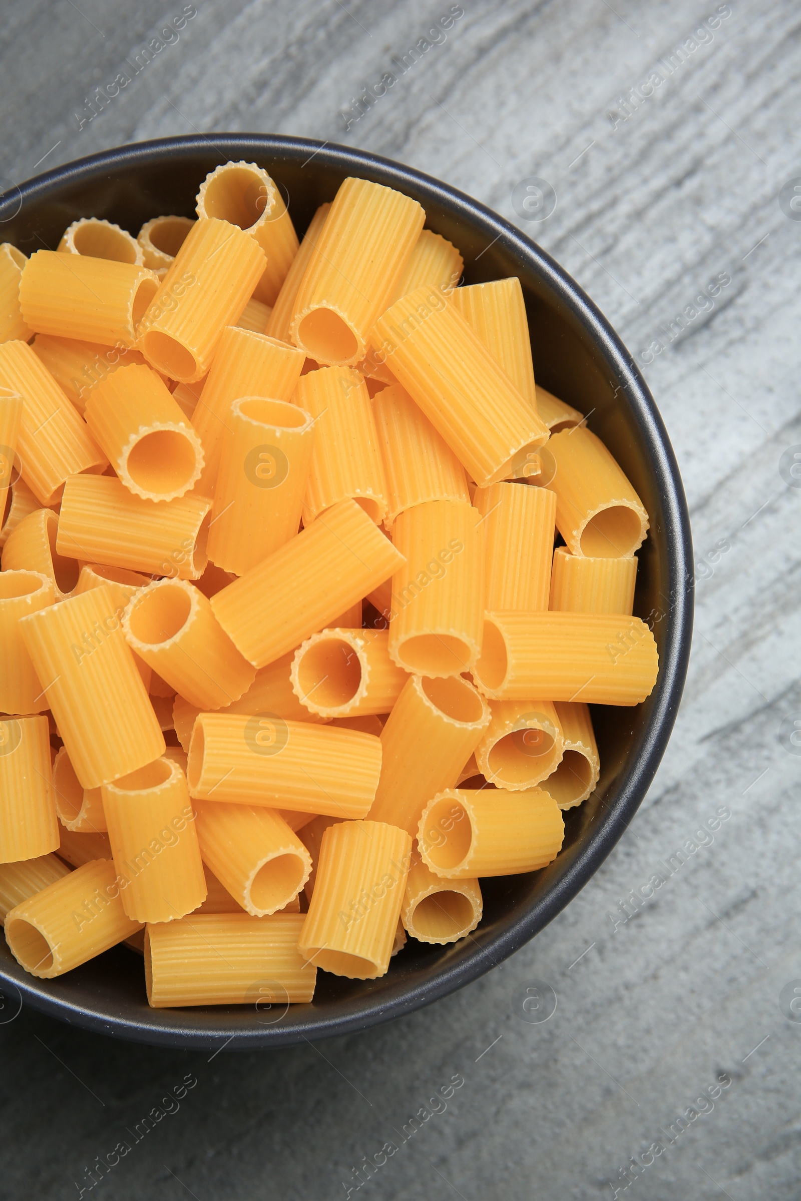 Photo of Raw rigatoni pasta in bowl on grey table, top view