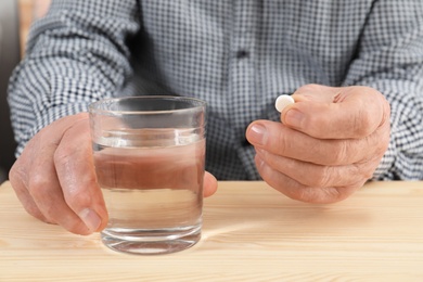 Photo of Senior man holding pill and glass of water at table, closeup