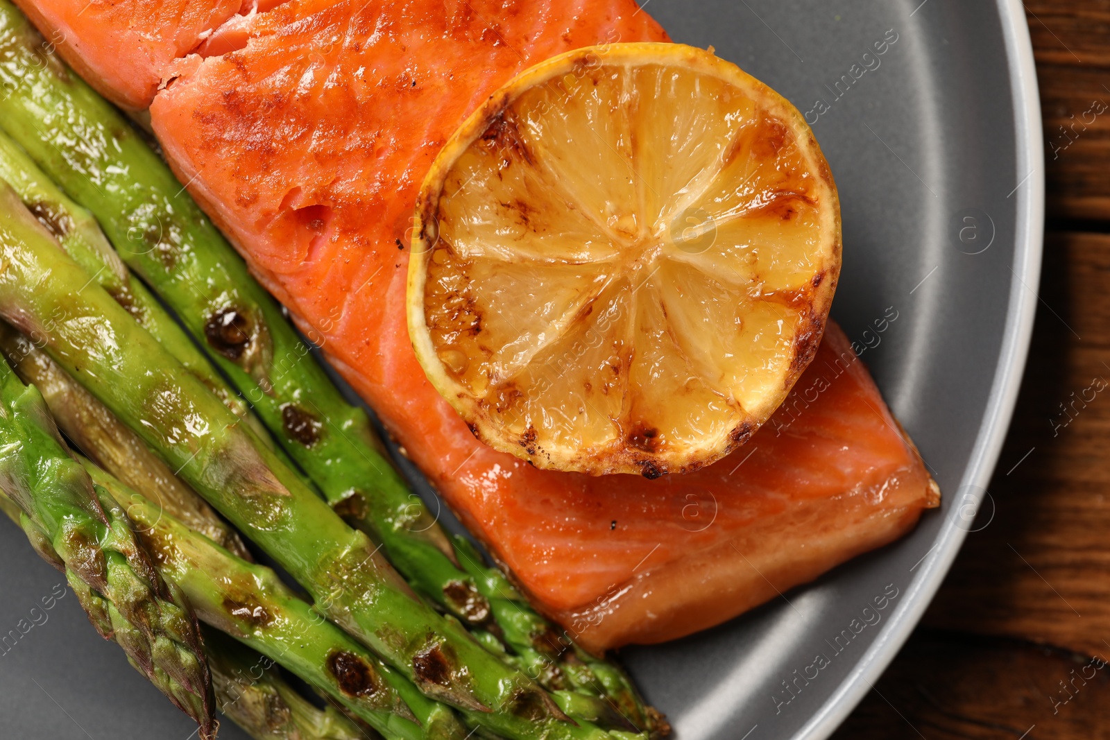 Photo of Tasty grilled salmon with asparagus and lemon on wooden table, top view