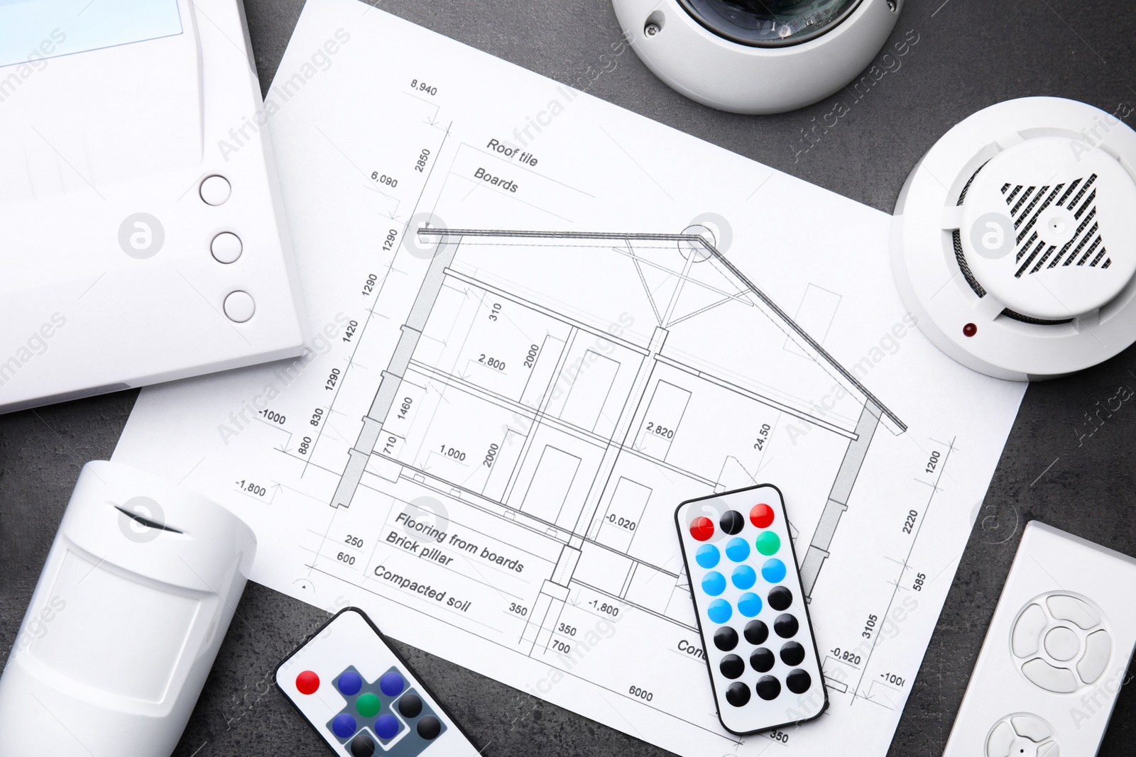 Photo of Building plan, remote controls, smoke and movement detectors on grey table, flat lay. Home security system