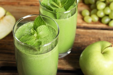 Photo of Green smoothie in glasses and fresh ingredients on wooden table, closeup