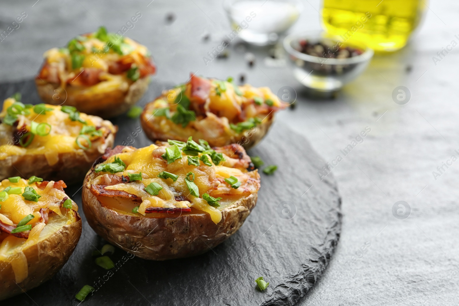 Photo of Slate plate with baked potatoes on table, closeup. Space for text