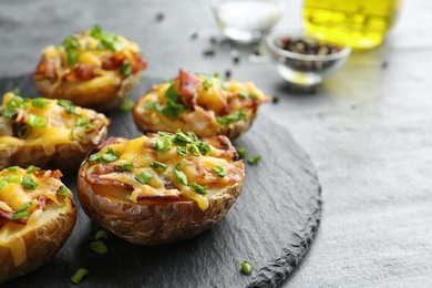 Photo of Slate plate with baked potatoes on table, closeup. Space for text