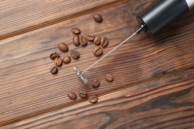 Black milk frother wand and coffee beans on wooden table, top view