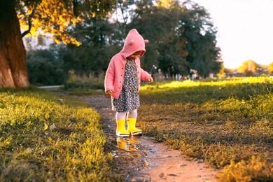 Little girl wearing rubber boots standing in puddle outdoors. Autumn walk