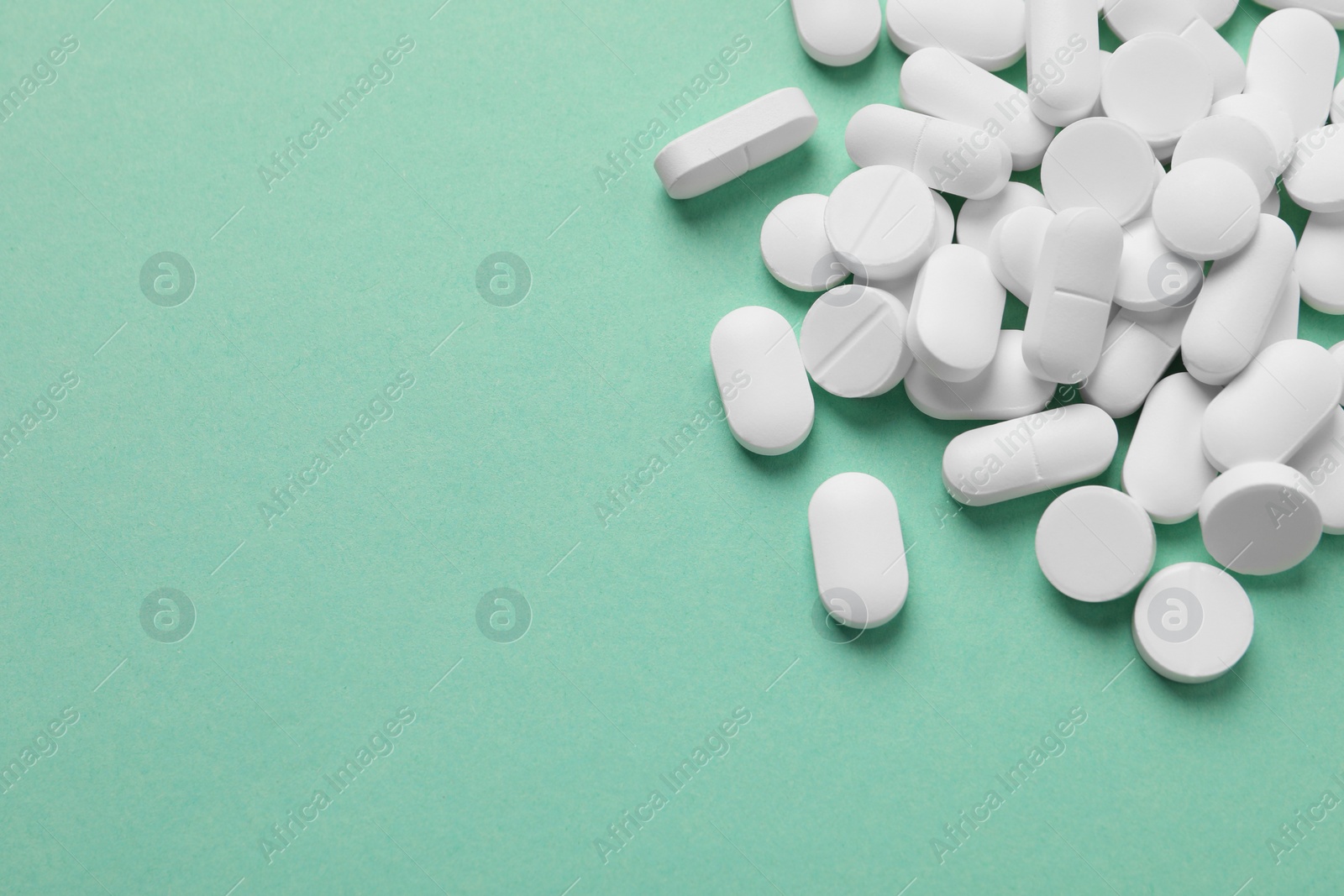 Photo of Pile of white pills on green background, flat lay. Space for text