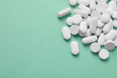 Photo of Pile of white pills on green background, flat lay. Space for text