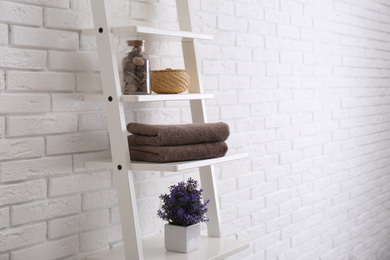 Photo of Clean soft towels and plant on shelves near white brick wall. Space for text