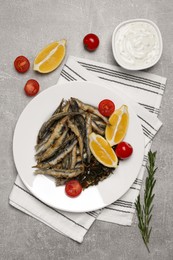 Photo of Delicious fried anchovies with cherry tomatoes and slices of lemon served on light grey table, flat lay