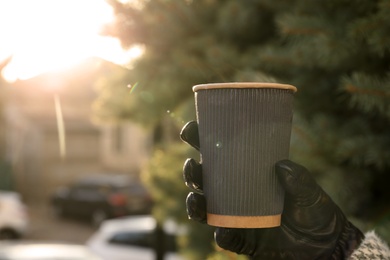 Photo of Woman with hot drink in paper cup outdoors, closeup. Space for text
