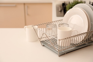 Photo of Dish drainer with clean dinnerware on table in kitchen. Space for text