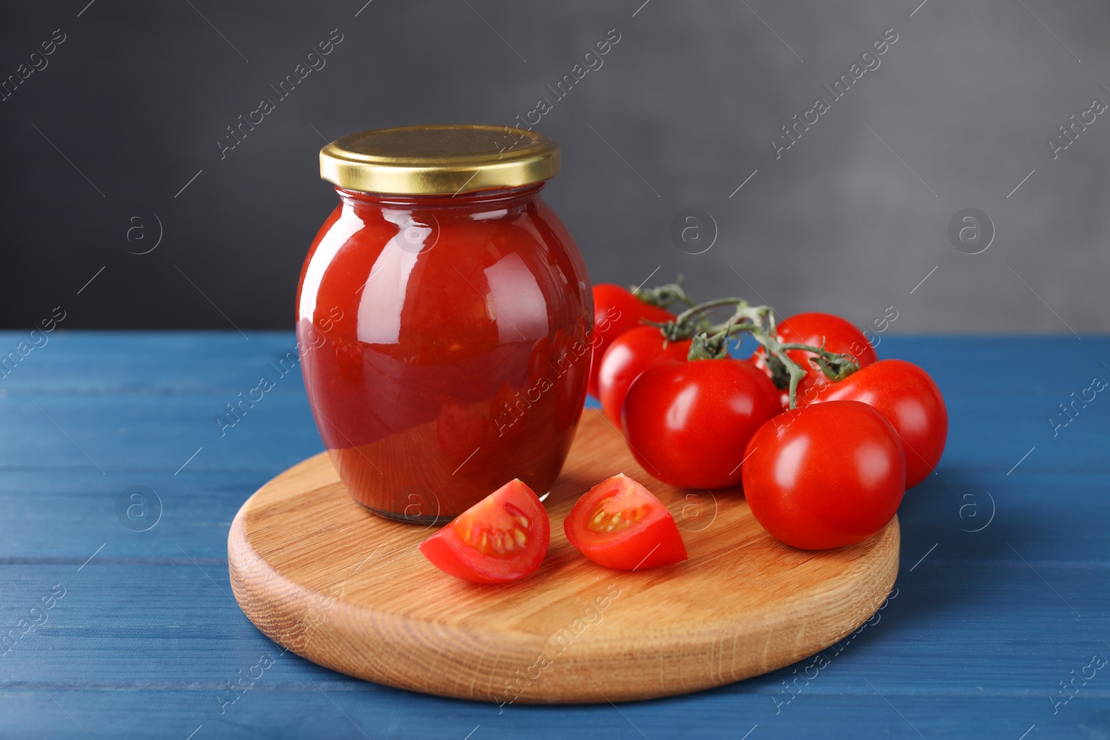 Photo of Organic ketchup in jar and fresh tomatoes on blue wooden table. Tomato sauce