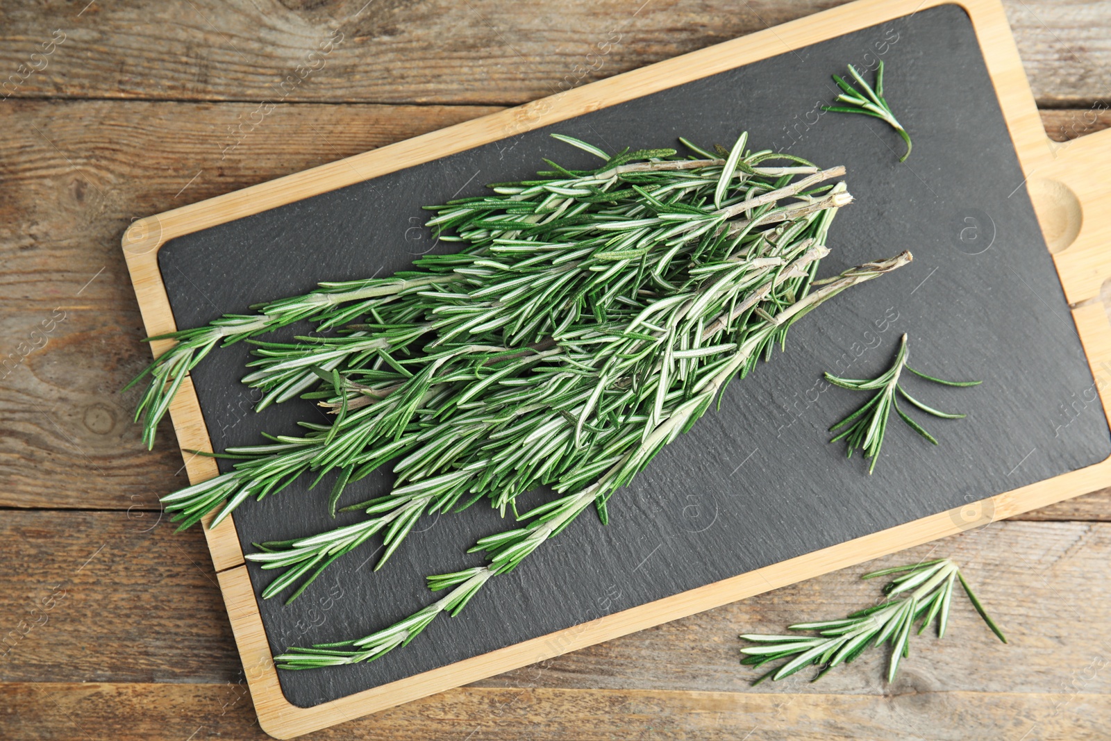 Photo of Board with fresh rosemary twigs on wooden table, top view