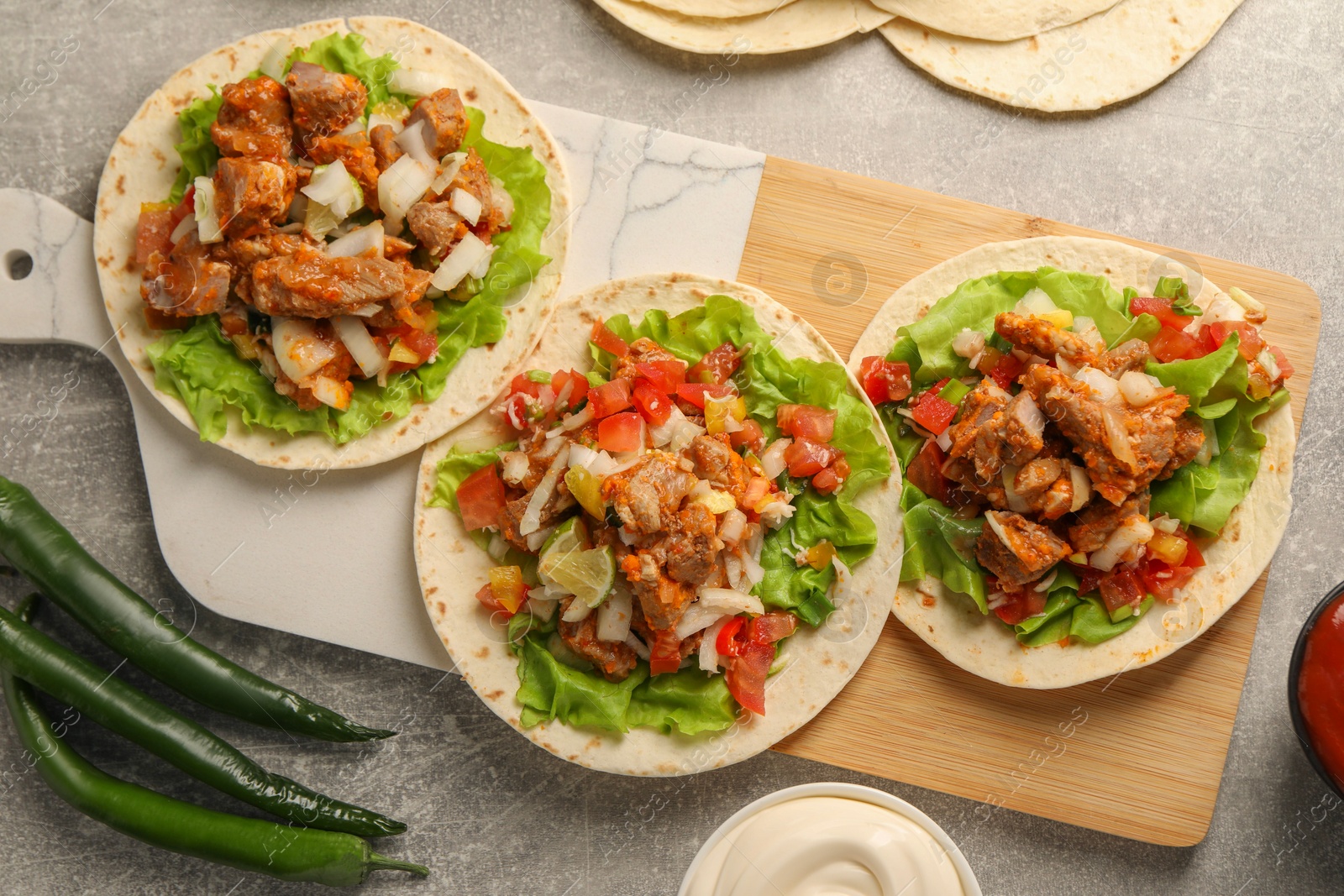 Photo of Delicious tacos with vegetables and meat on grey textured table, flat lay