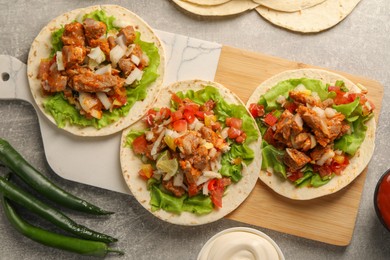 Delicious tacos with vegetables and meat on grey textured table, flat lay