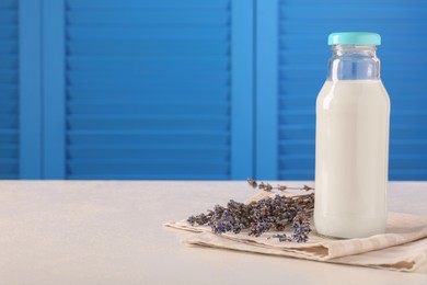 Bottle of tasty milk and lavender flowers on table against light blue wall, space for text