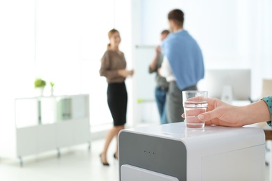 Photo of Office employee with glass near water cooler at workplace, closeup. Space for text