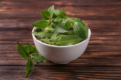 Photo of Fresh green bay leaves in bowl on wooden table