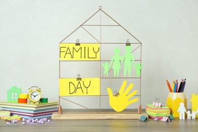 Photo of Paper cutout, palm and cards with text Family Day attached to decorative house on wooden table