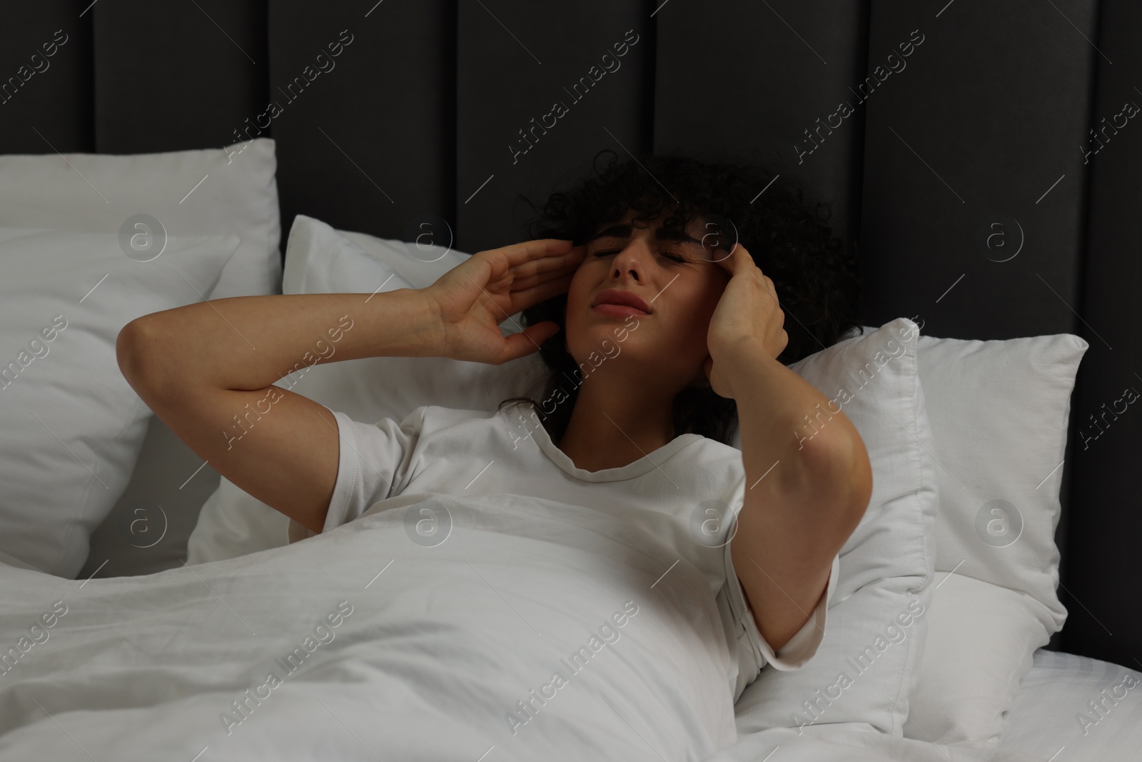 Photo of Young woman suffering from headache in bed at night