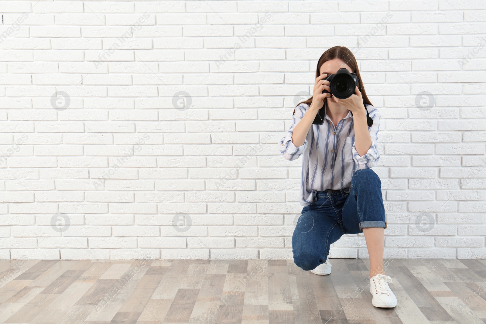 Photo of Professional photographer taking picture near white brick wall. Space for text