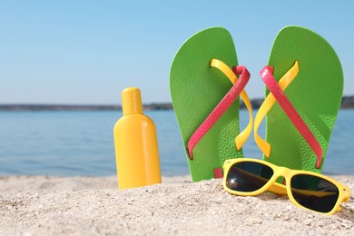 Photo of Stylish flip flops, sunglasses and sun protection cream on sandy beach