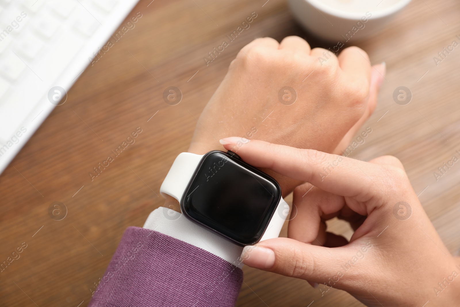 Image of Woman checking stylish smart watch at wooden table, top view