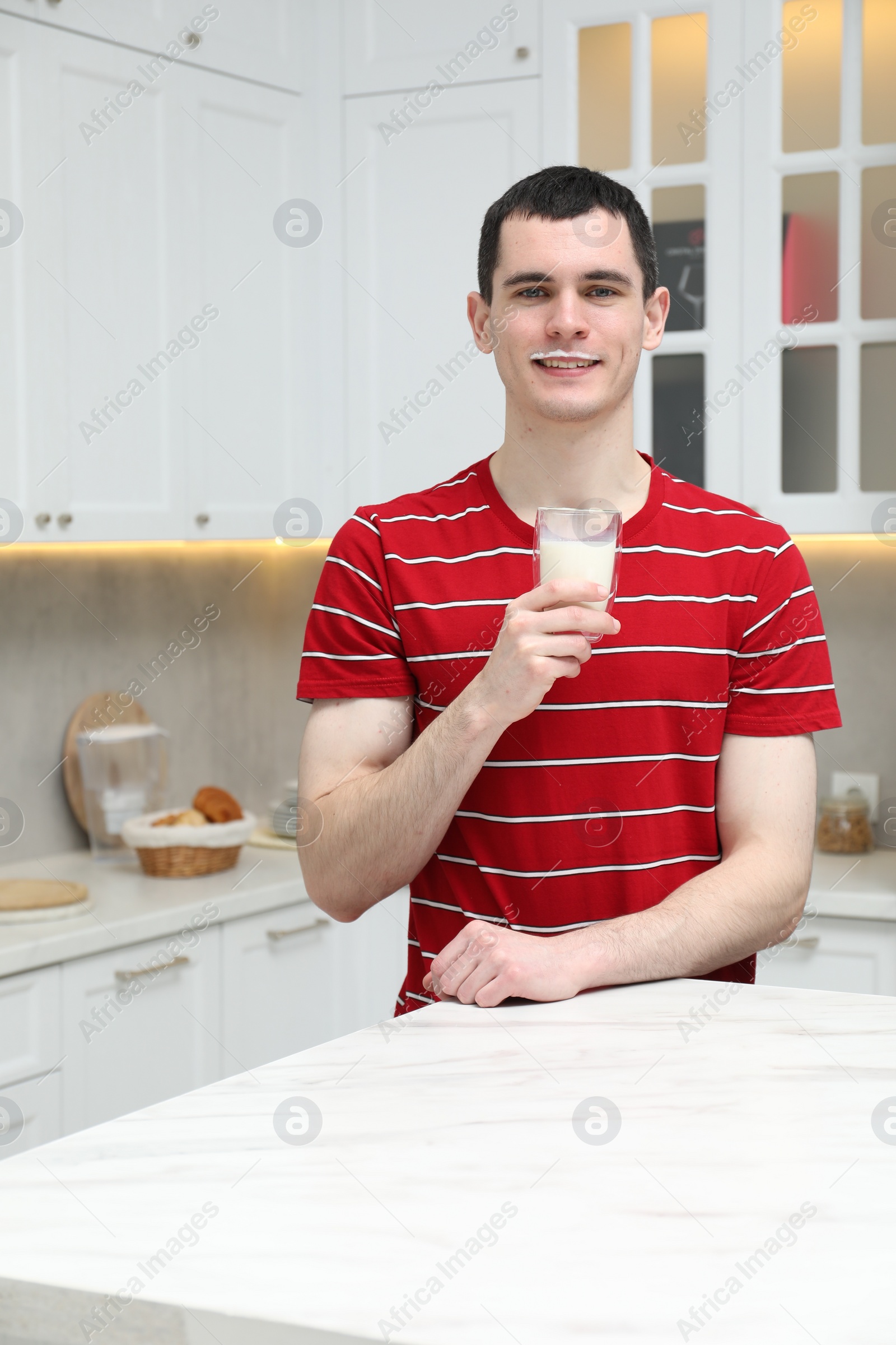 Photo of Happy man with milk mustache holding glass of tasty dairy drink in kitchen