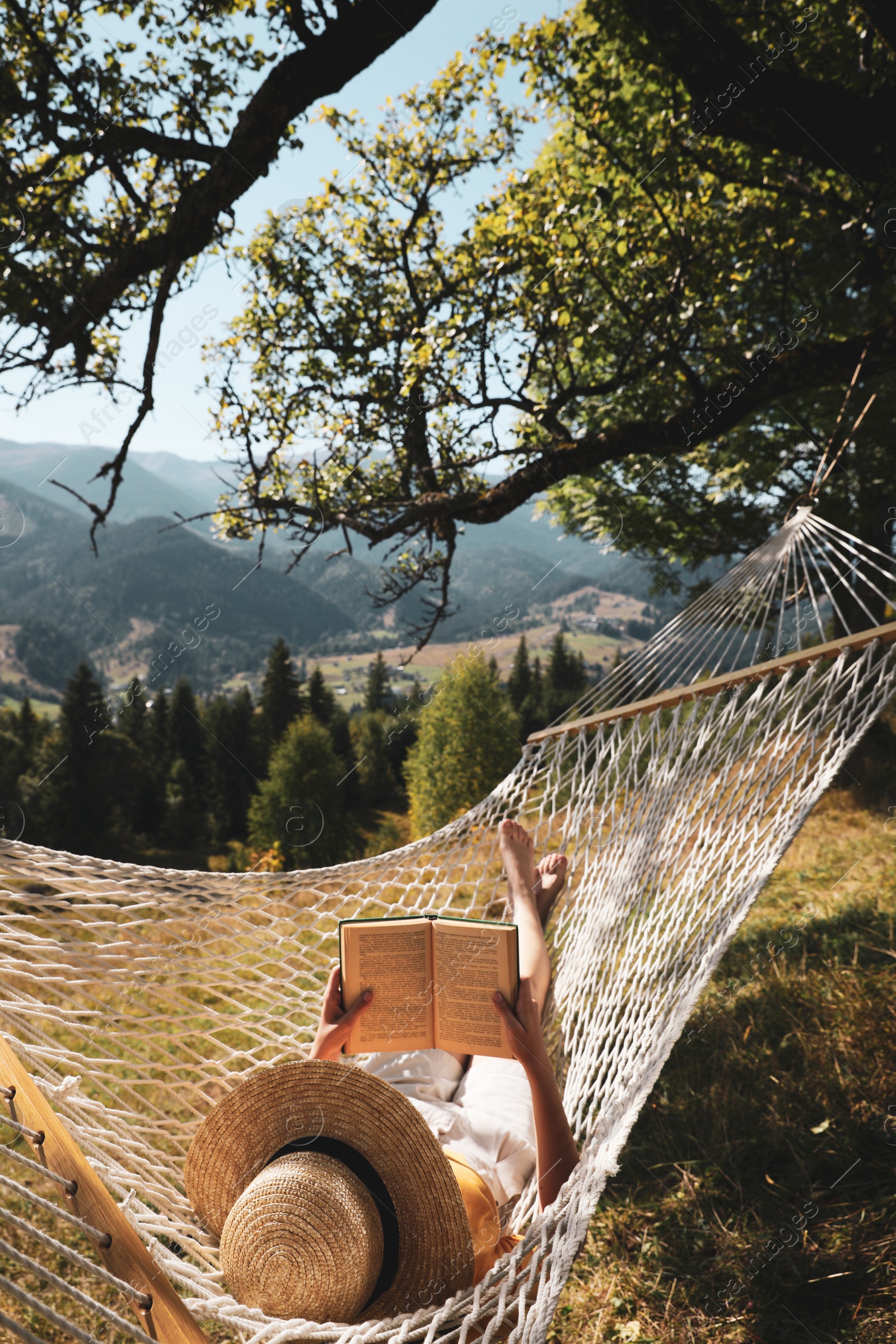 Photo of Young woman reading book in hammock outdoors on sunny day