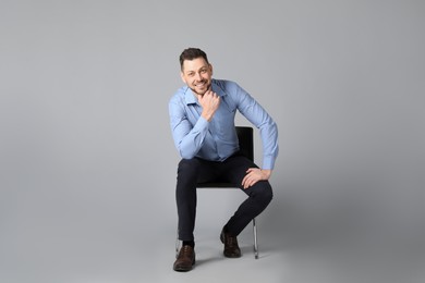 Handsome man sitting in office chair on grey background