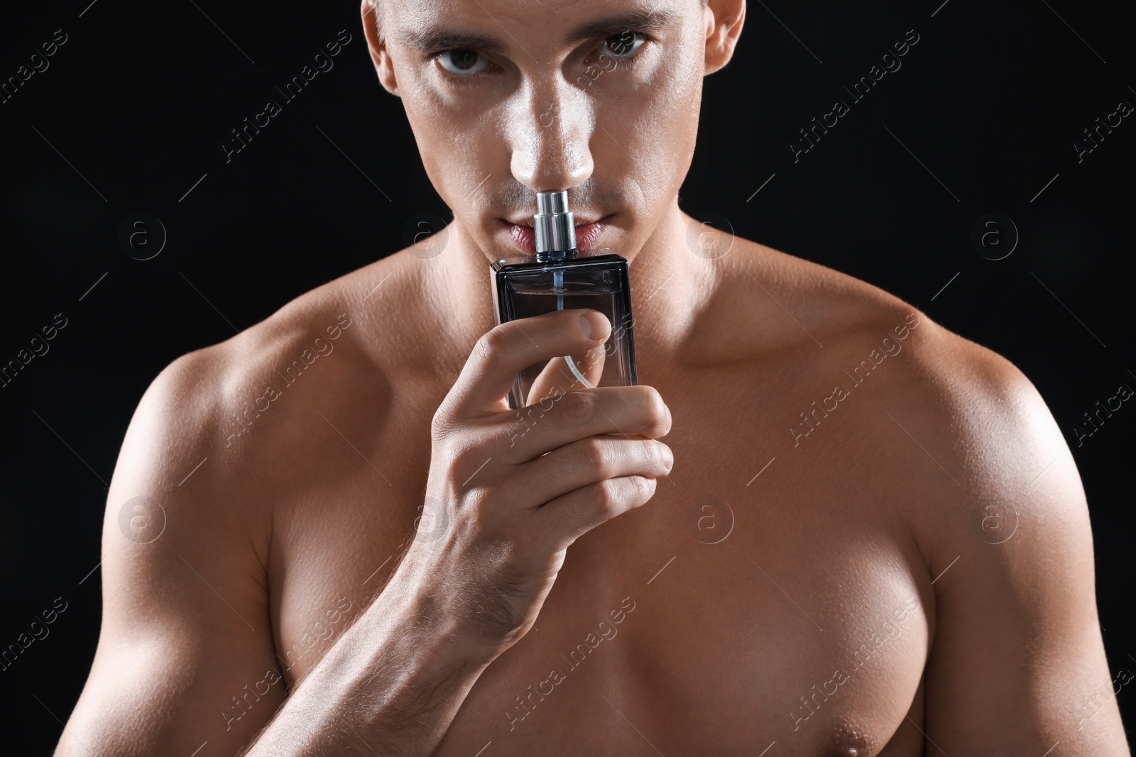 Photo of Handsome young man smelling bottle of perfume on black background