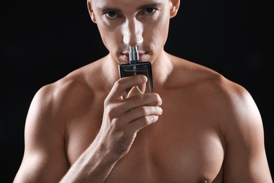 Photo of Handsome young man smelling bottle of perfume on black background